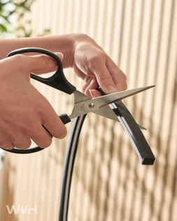 Person using scissors to cut RGB LED light strip in front of slat panel wall